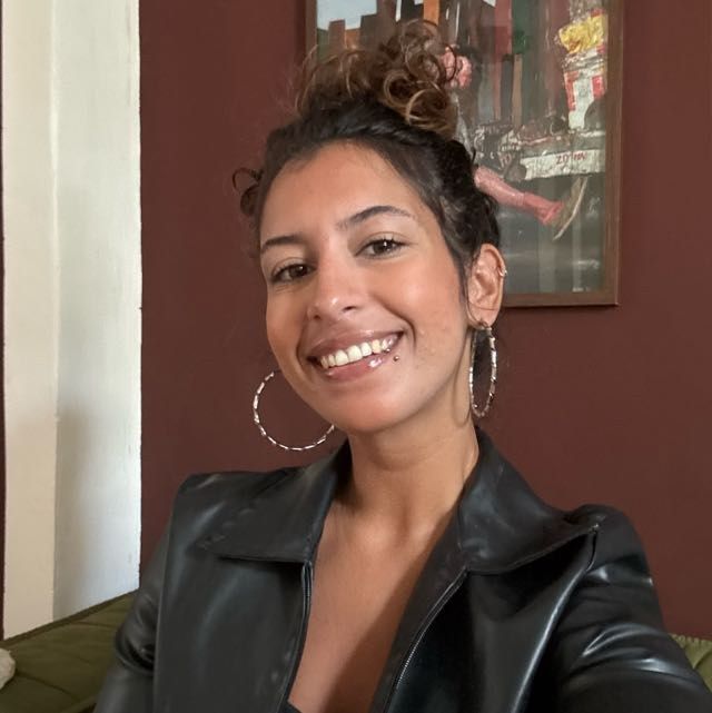 Retrato de Júlia Corrêa, sorrindo, de cabelo preso e jaqueta preta.